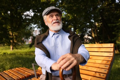 Photo of Handsome elderly man with walking cane sitting on bench outdoors
