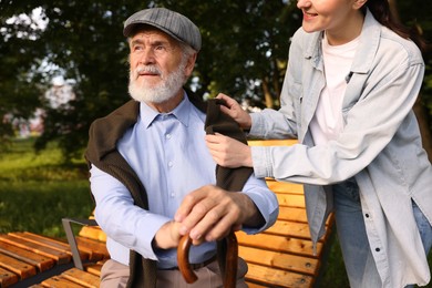 Photo of Smiling caregiver supporting elderly man with walking cane outdoors, closeup