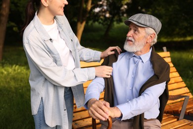 Photo of Smiling caregiver supporting elderly man with walking cane outdoors, closeup