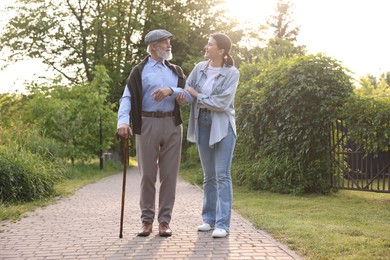 Photo of Smiling caregiver supporting elderly man with walking cane outdoors