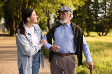 Photo of Smiling caregiver supporting elderly man with walking cane outdoors