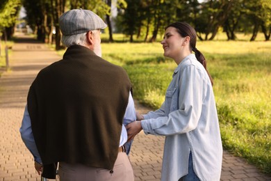 Photo of Smiling caregiver supporting elderly man in park
