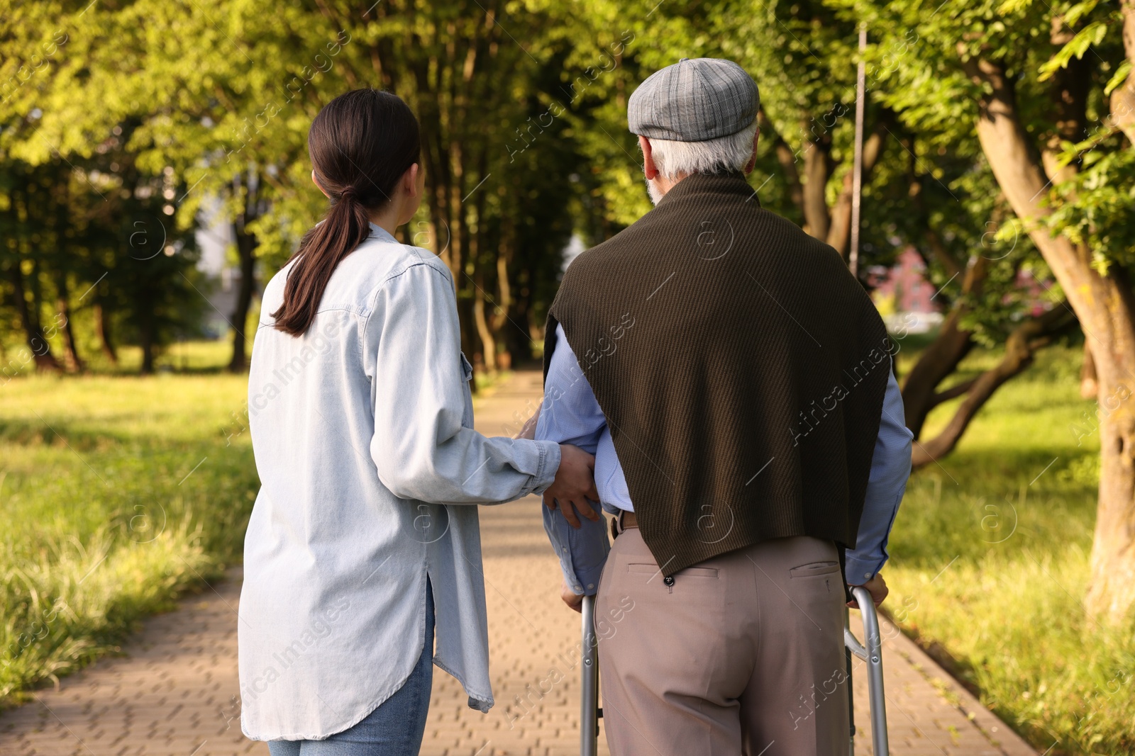 Caregiver supporting elderly man who using walking frame outdoors, back view Photo of Caregiver supporting elderly man who using walking frame outdoors, back view
