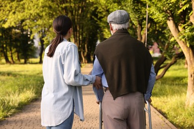 Photo of Caregiver supporting elderly man who using walking frame outdoors, back view