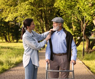 Photo of Smiling caregiver supporting elderly man who using walking frame outdoors