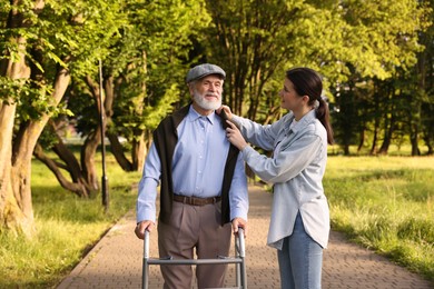 Photo of Smiling caregiver supporting elderly man who using walking frame outdoors