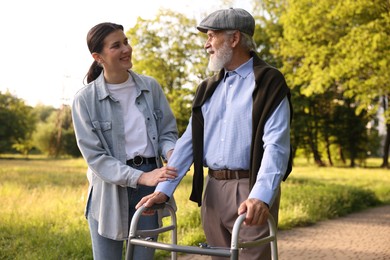 Photo of Smiling caregiver supporting elderly man who using walking frame outdoors