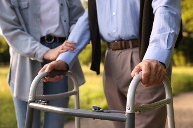 Photo of Caregiver supporting elderly man who using walking frame outdoors, closeup
