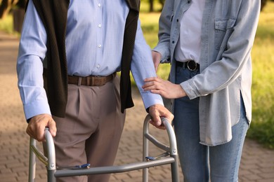 Photo of Caregiver supporting elderly man who using walking frame outdoors, closeup