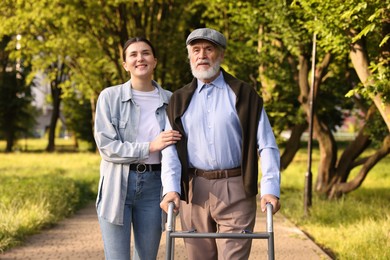 Photo of Smiling caregiver supporting elderly man who using walking frame outdoors