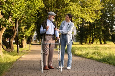Photo of Smiling caregiver supporting elderly man who using walking frame outdoors