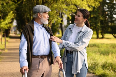 Photo of Smiling caregiver supporting elderly man who using walking frame outdoors