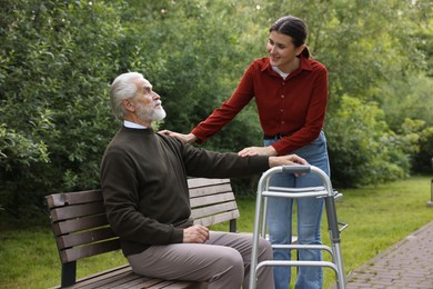 Photo of Smiling caregiver supporting elderly man with walking frame outdoors