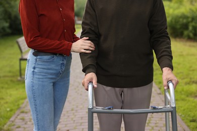 Photo of Caregiver supporting elderly man who using walking frame outdoors, closeup