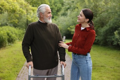 Photo of Caregiver supporting elderly man who using walking frame outdoors