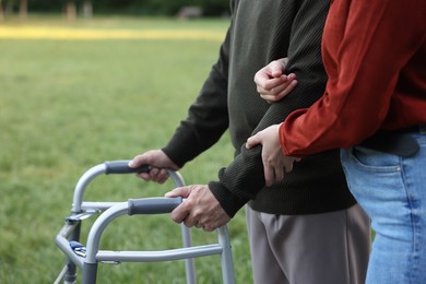 Photo of Caregiver supporting elderly man who using walking frame outdoors, closeup