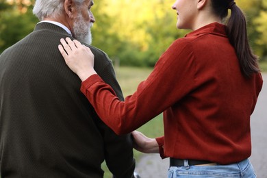 Photo of Caregiver supporting elderly man outdoors, back view