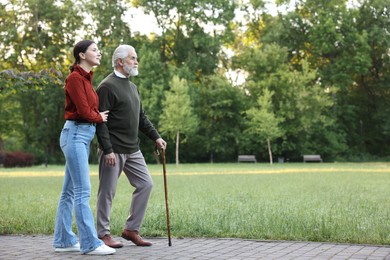 Photo of Smiling caregiver supporting elderly man who using walking cane outdoors. Space for text