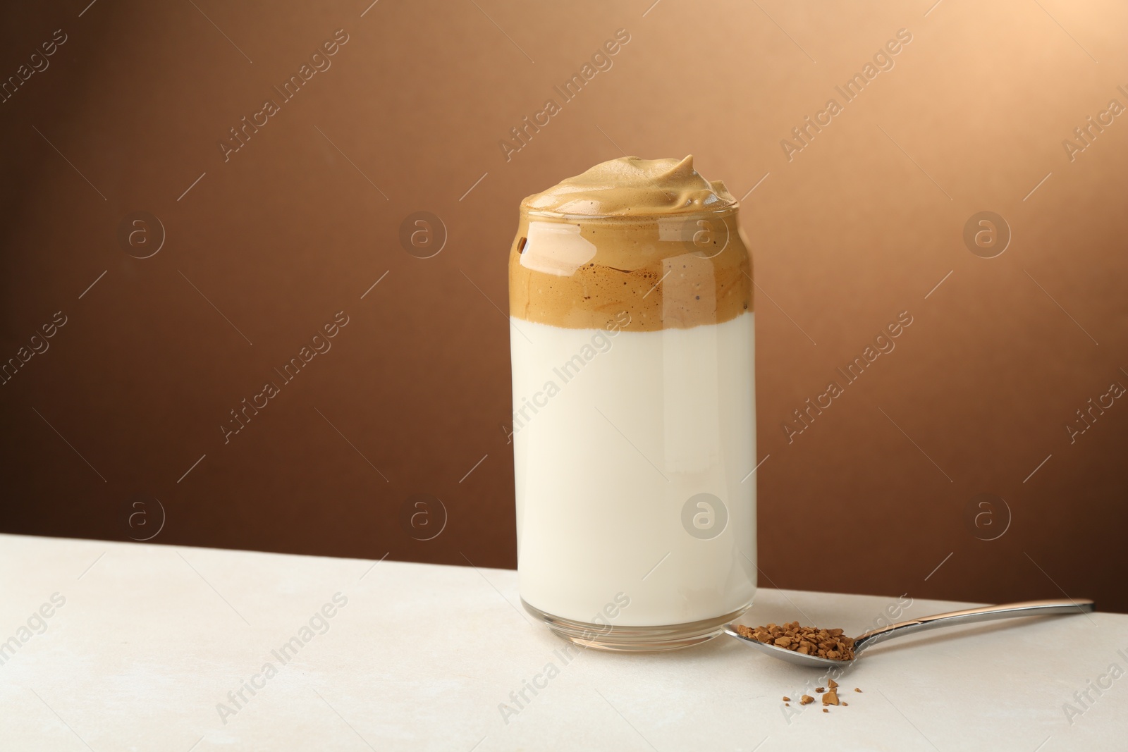 Photo of Delicious dalgona coffee in glass and granules on white table, space for text