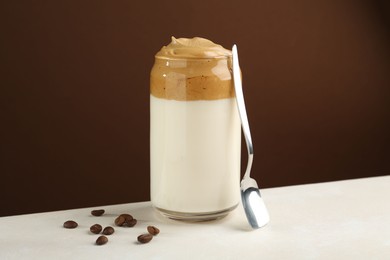Photo of Delicious dalgona coffee in glass, beans and spoon on white table