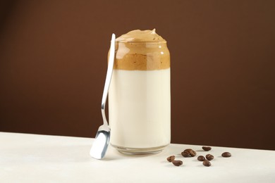 Photo of Delicious dalgona coffee in glass, beans and spoon on white table