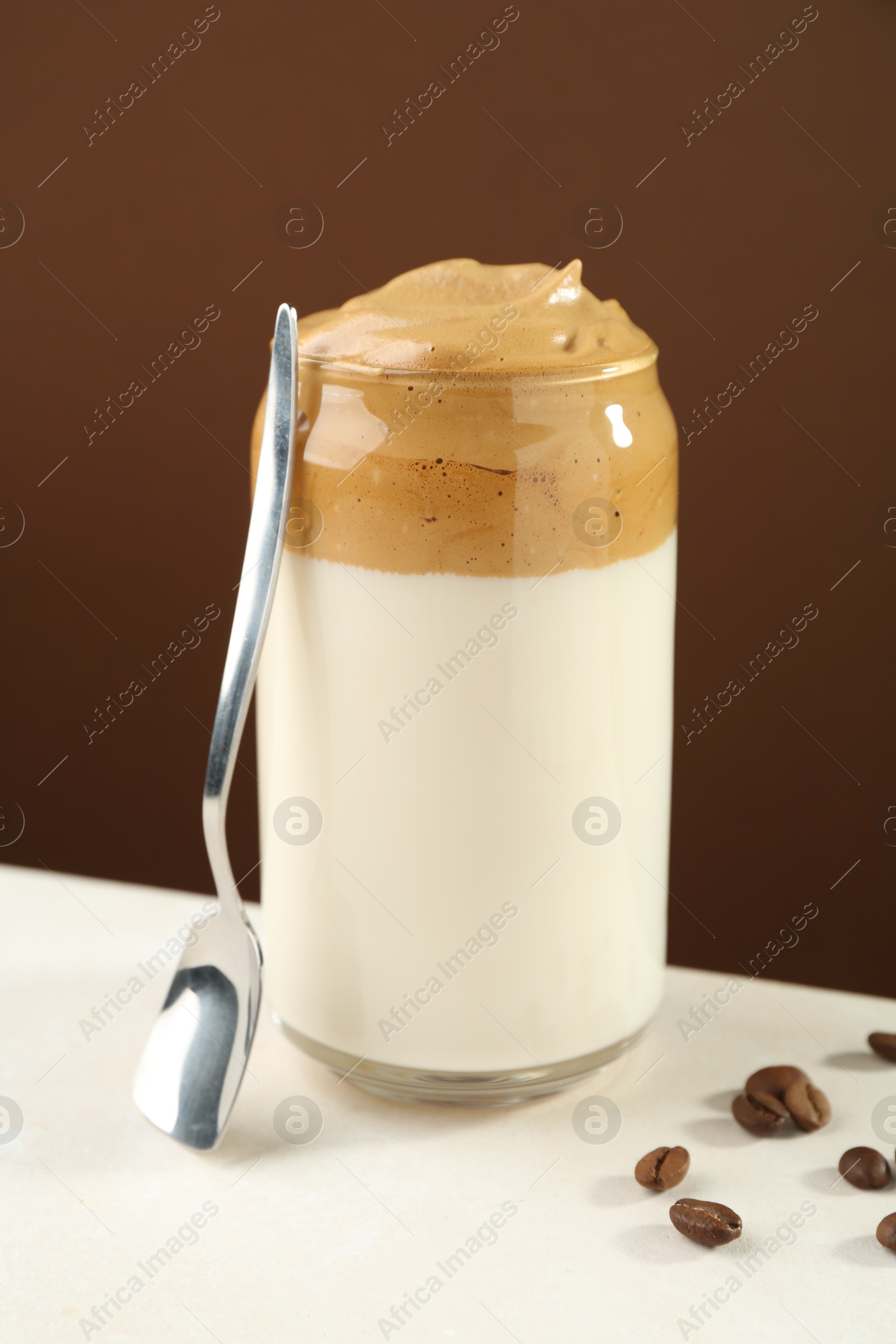 Photo of Delicious dalgona coffee in glass, beans and spoon on white table