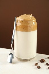 Photo of Delicious dalgona coffee in glass, beans and spoon on white table