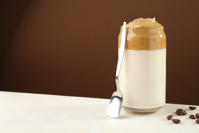 Photo of Delicious dalgona coffee in glass, beans and spoon on white table, space for text