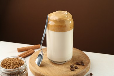 Photo of Delicious dalgona coffee in glass, beans, granules and cinnamon on white table, closeup