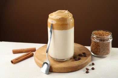 Photo of Delicious dalgona coffee in glass, beans, granules and cinnamon on white table