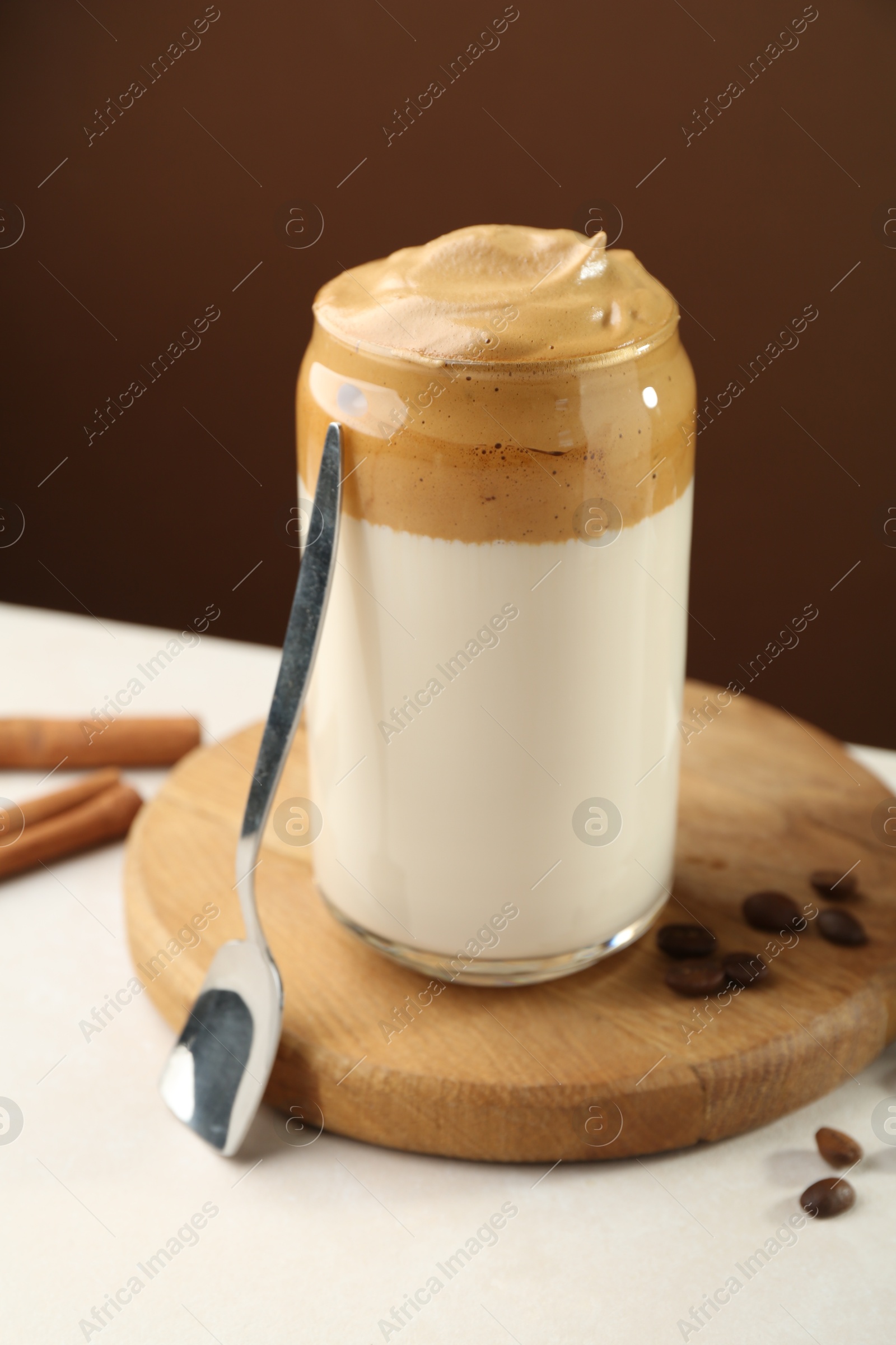 Photo of Delicious dalgona coffee in glass, beans and cinnamon on white table, closeup