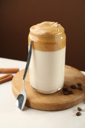 Photo of Delicious dalgona coffee in glass, beans and cinnamon on white table, closeup