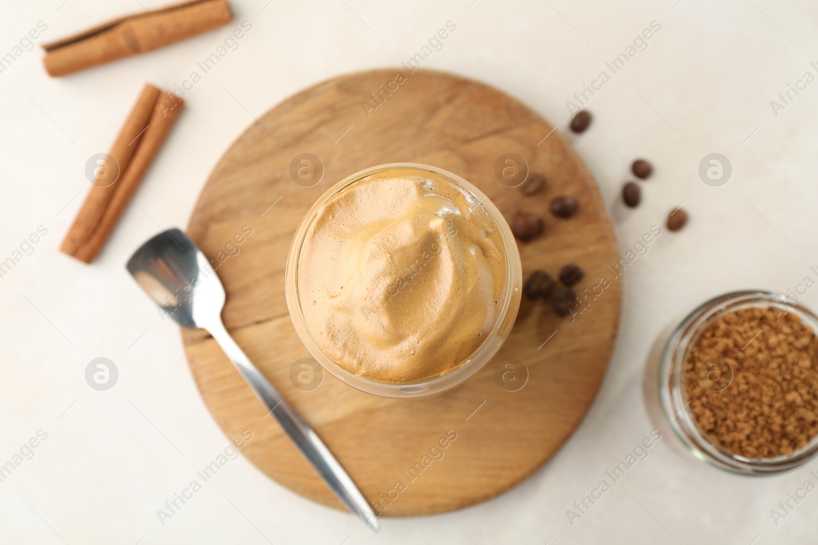 Photo of Delicious dalgona coffee in glass, beans, granules and cinnamon on white table, flat lay