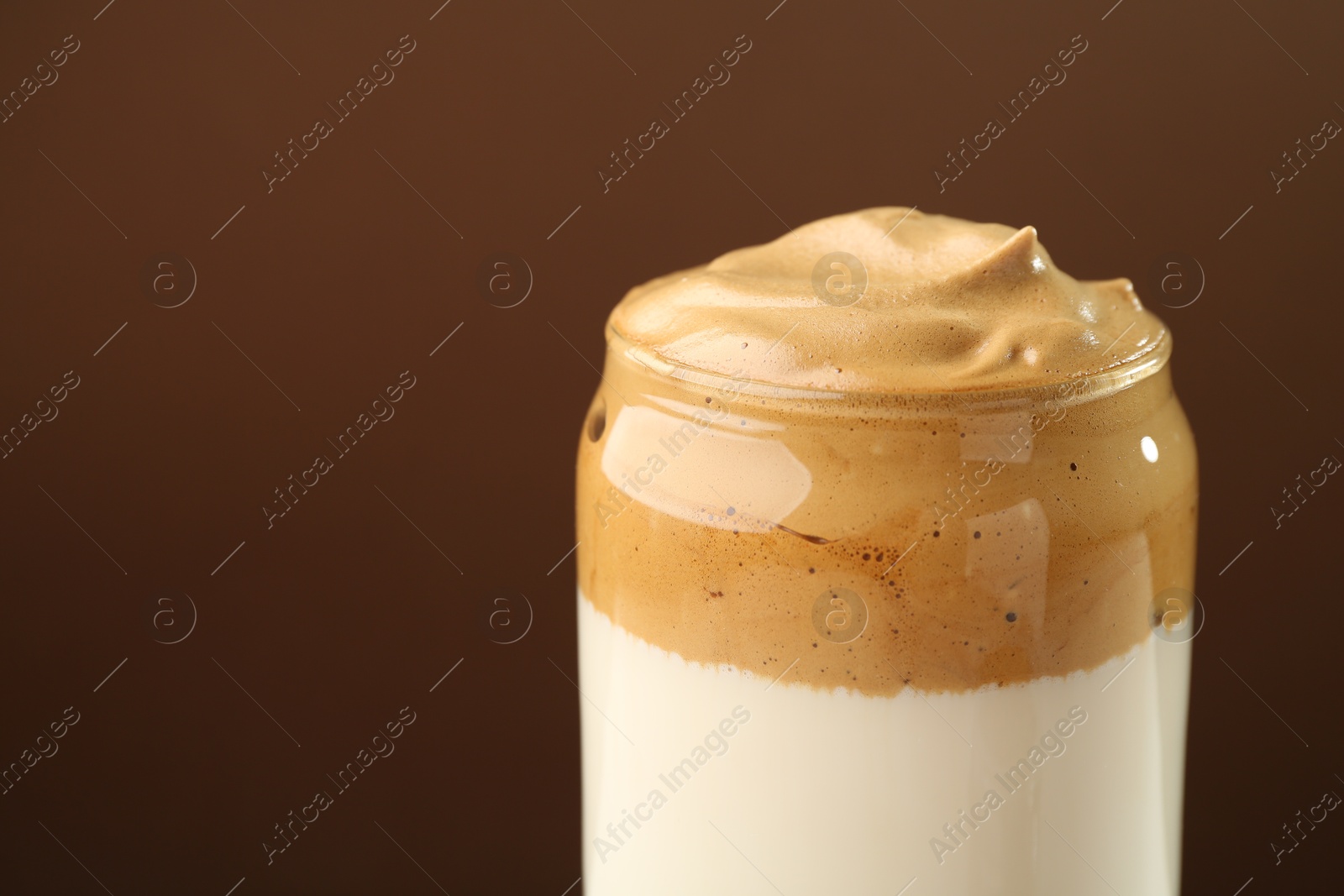 Photo of Delicious dalgona coffee in glass on brown background, closeup. Space for text