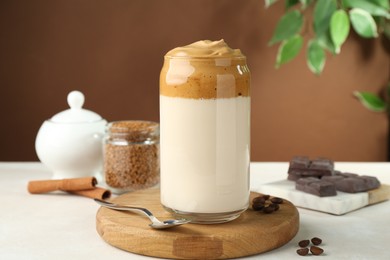 Photo of Delicious dalgona coffee in glass, beans, granules, chocolate and cinnamon on white table