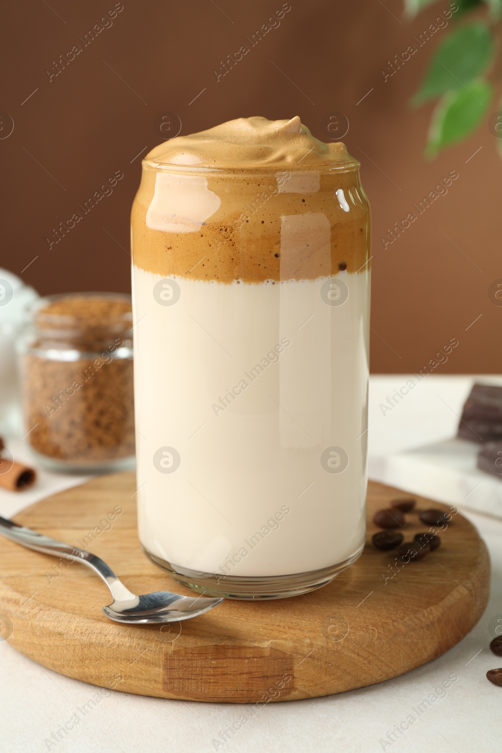 Photo of Delicious dalgona coffee in glass, beans and granules on white table, closeup