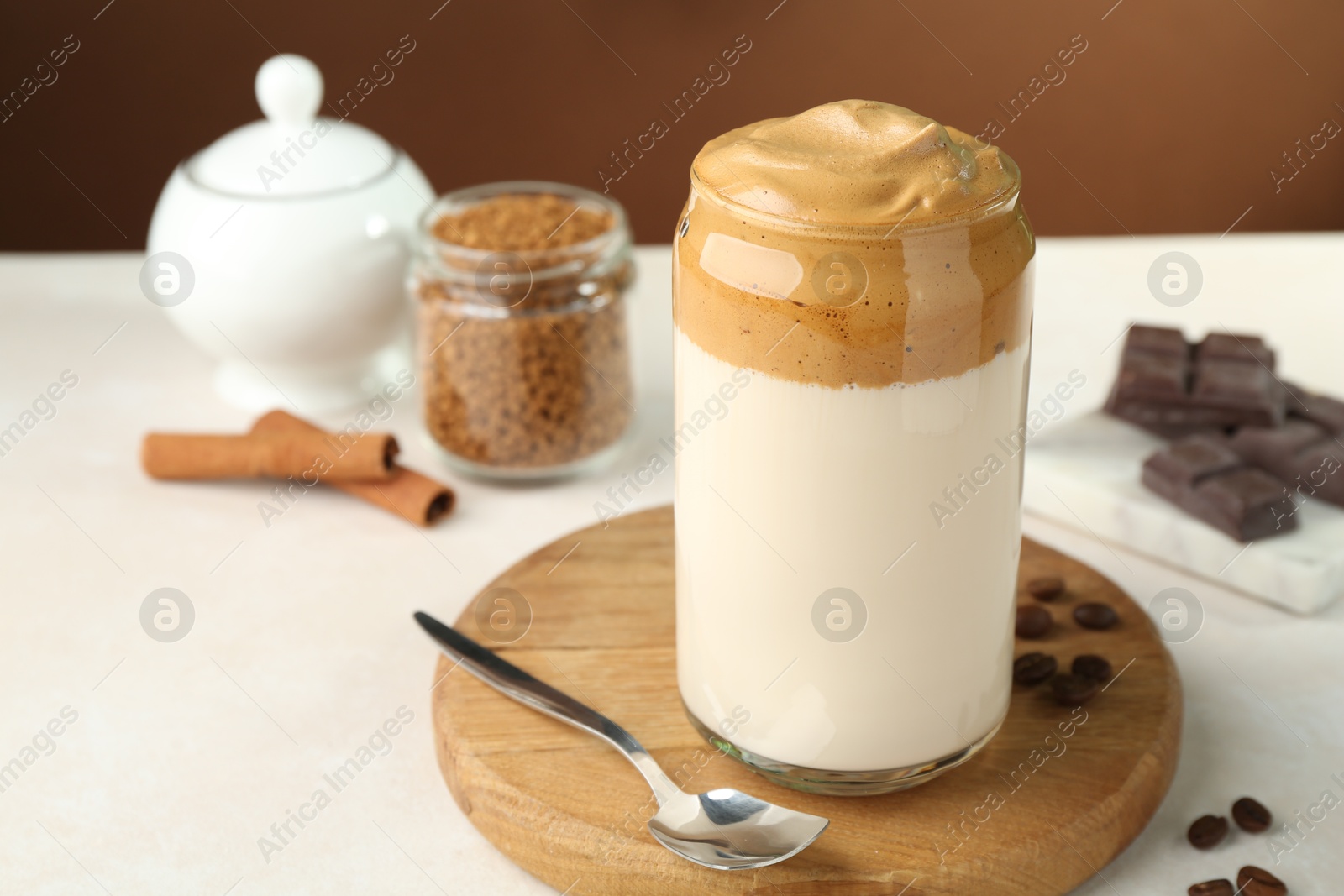 Photo of Delicious dalgona coffee in glass, beans, granules, chocolate and cinnamon on white table, closeup