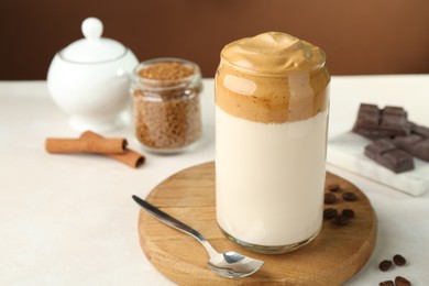 Photo of Delicious dalgona coffee in glass, beans, granules, chocolate and cinnamon on white table, closeup