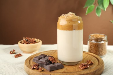 Photo of Delicious dalgona coffee in glass, pieces of chocolate, walnuts and granules on table, closeup