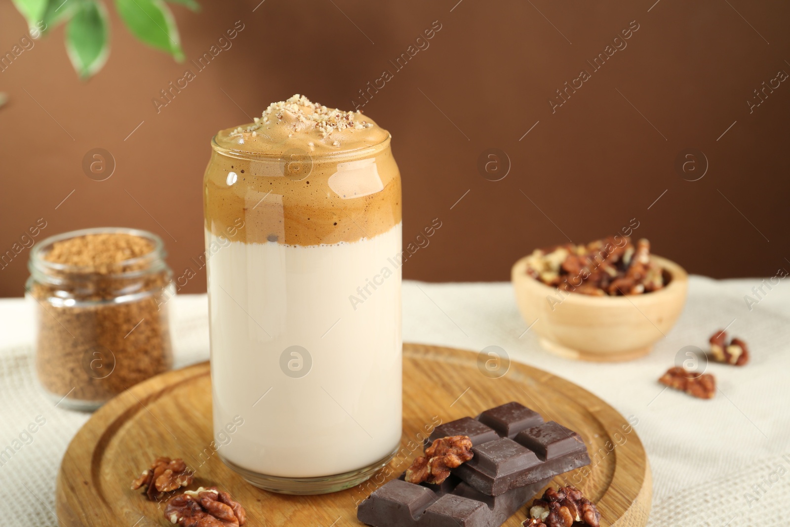 Photo of Delicious dalgona coffee in glass, pieces of chocolate, walnuts and granules on table, closeup