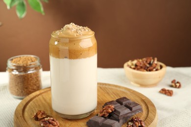Photo of Delicious dalgona coffee in glass, pieces of chocolate, walnuts and granules on table, closeup