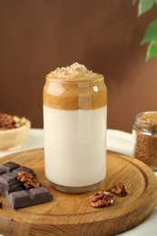 Photo of Delicious dalgona coffee in glass, pieces of chocolate and walnuts on table, closeup