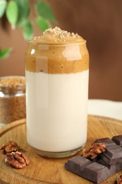 Photo of Delicious dalgona coffee in glass, pieces of chocolate and walnuts on table, closeup