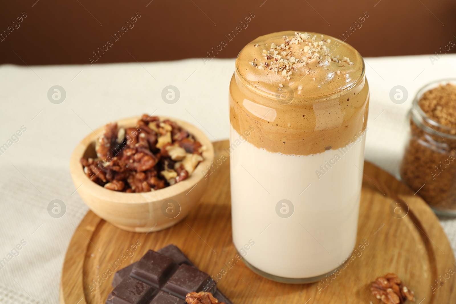 Photo of Delicious dalgona coffee in glass, pieces of chocolate, walnuts and granules on table, closeup