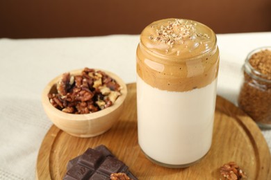 Photo of Delicious dalgona coffee in glass, pieces of chocolate, walnuts and granules on table, closeup