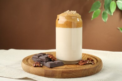 Photo of Delicious dalgona coffee in glass, pieces of chocolate and walnuts on table