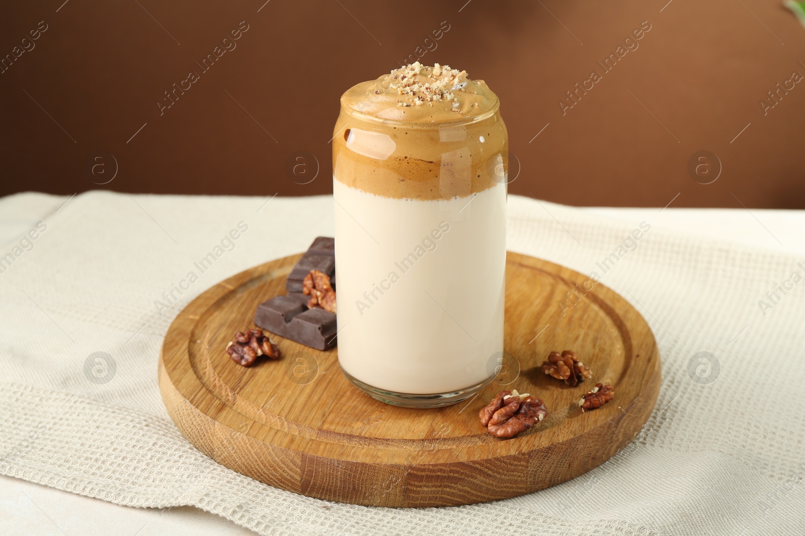 Photo of Delicious dalgona coffee in glass, pieces of chocolate and walnuts on table