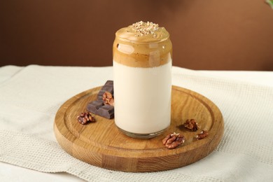 Photo of Delicious dalgona coffee in glass, pieces of chocolate and walnuts on table