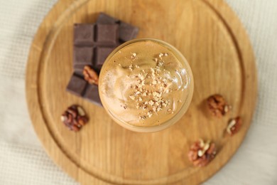 Photo of Delicious dalgona coffee in glass, pieces of chocolate and walnuts on table, top view