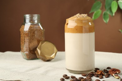 Photo of Delicious dalgona coffee in glass, beans, walnuts and granules on table, closeup